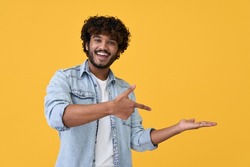 Excited happy positive young indian man student pointing aside with fingers hand gesture at copy space advertising product, presenting sale discount promo offer standing isolated on yellow background.
