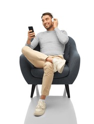 technology, people and music concept - happy smiling man with smartphone and earphones sitting in chair over white background