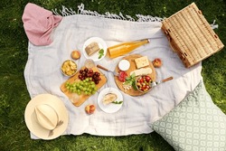 leisure and eating concept - close up of food, drinks and picnic basket on blanket on grass at summer park