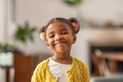 Smiling cute little african american girl with two pony tails looking at camera. Portrait of happy female child at home. Smiling face a of black 4 year old girl looking at camera with afro puff hair.