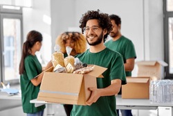 charity, donation and volunteering concept - happy smiling male volunteer with food in box and international group of people at distribution or refugee assistance center