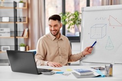 distant education, school and remote job concept - happy smiling male math teacher with laptop compute showing geometric shapes on flip chart having online class or video call at home office
