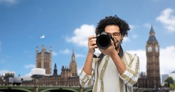 travel, tourism and people and concept - happy smiling man, photographer or tourist in glasses with digital camera over london city, england background