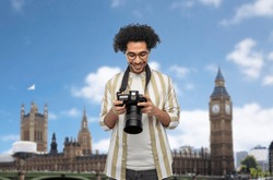 travel, tourism and people and concept - happy smiling man, photographer or tourist in glasses with digital camera over london city, england background