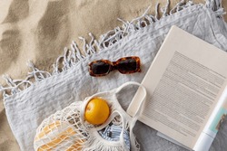 leisure and summer holidays concept - bag of oranges, sunglasses and magazine on blanket on beach sand