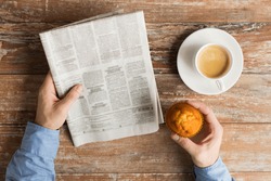 business, information, people and mass media concept - close up of male hands with newspaper, muffin and coffee cup on table