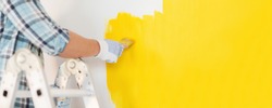 repair and home renovation concept - close up of male hand in gloves painting a wall with yellow paint