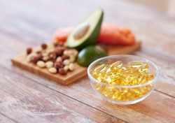 healthy eating, diet and omega 3 nutritional supplements concept - close up of cold liver oil capsules in glass bowl and food on table