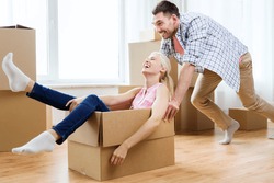 home, people, moving and real estate concept - happy couple having fun and riding in cardboard boxes at new home