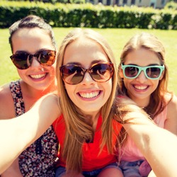 friendship, leisure, summer, technology and people concept - group of smiling teen girls taking selfie with smartphone camera or tablet pc in park