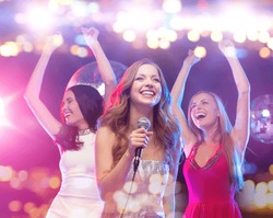 party, holidays, nightlife, entertainment and people concept - concept - happy women with microphone singing karaoke and dancing at night club