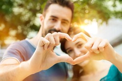 Closeup shot of young man and woman making heart shape with hand. Loving couple making heart shape with hands outdoor. Female and male hands making up heart shape.