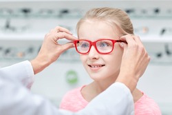 optician putting glasses to girl at optics store