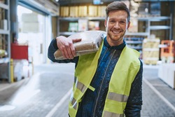 Smiling young man working in a warehouse standing with a bag of product over his shoulder grinning happily at the camera, close up view