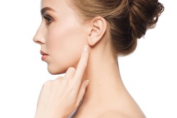 health, people and beauty concept - beautiful young woman pointing finger to her ear over white background