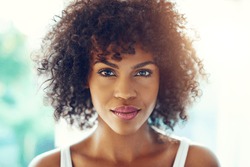 Portrait of young afro-american pretty girl looking at camera on blurred inside background. 