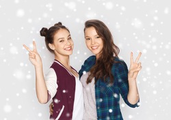 winter, christmas, people, teens and friendship concept - happy smiling pretty teenage girls or friends hugging and showing peace hand sign over gray background and snow