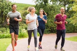 Healthy group of people jogging on track in park. Happy couple enjoying friend time at jogging park while running. Mature friends running together outdoor.