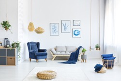 White living room with wood sofa, blue armchair, lamps, posters