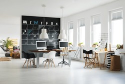 Modern workspace with blackboard calendar, desk, chairs and computers