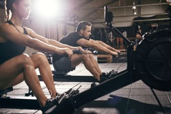 Side view of man and woman doing exercises with rowing machine at gym.