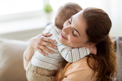 family, child and motherhood concept - happy smiling young mother hugging little baby at home