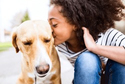 African american girl outdoors with her dog, kissing him.