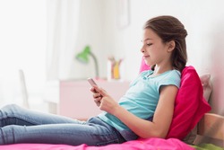children, technology and communication concept - smiling girl texting on smartphone and lying in bed at home