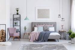 Comfortable powder pink chair next to shelf with firewood in soft pastel bedroom with decorative glass vases