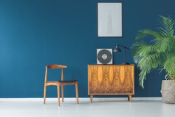 Stylish apartment interior with blue wall decorated in vintage style with wooden cupboard,chair, mock-up poster and tropical potted plant