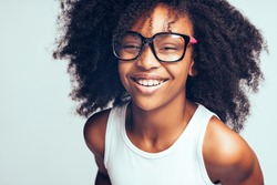 Smiling young African girl with long curly hair wearing glasses while standing by herself against a gray background