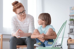 Young female school psychologist having serious conversation with smart little boy at her office