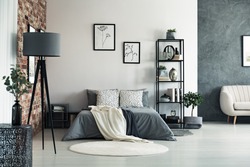 Vase on metal table and grey lamp in spacious bedroom with white carpet and gallery on wall above bed