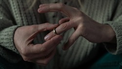 Wrinkled Caucasian Female Hands Taking Off a Wedding Ring and Debating Whether to Get a Divorce or Not. Female Wearing a Light Colored Sweater.