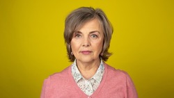 Neutral Elderly Woman in an Isolated Yellow Background Setting Looking Directly in the Camera. Feeling Tired.