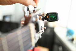 Tuner is installed on guitar neck for tuning notes. Tuner for an acoustic guitar. Each string makes reference sound. Musician guitar workshop. Specialist will assist in improving tool