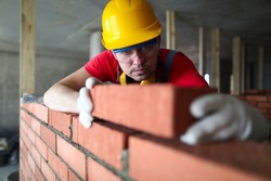 Builder carefully puts red brick on the masonry. Quick work bricklayer. Guy measures level masonry. Man is building brick wall. Correctly calculate material. Builder manually carries brick structure