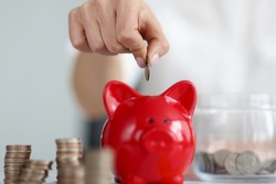 Female hand throwing cash coins into red piggy bank closeup. Home bookkeeping concept