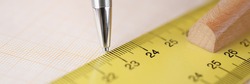 Ballpoint pen drawing line under ruler on graph paper closeup