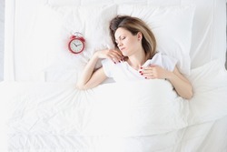 Young woman lying in bed near red alarm clock top view