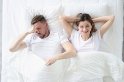 Married couple lying in bed. Man covering his nose with his hand