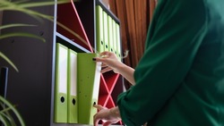 Green folders in office woman takes folder with documents from cabinet. Work with documentation and accounting