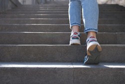 Close-up of female in jeans and sneakers going up steep stairs. Woman tourist in casual clothes going upstairs outdoors
