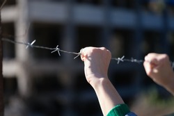 Close-up of woman hands holding metal security barbedwire fence. Wire with clusters of short, sharp spikes. Fence or warfare obstruction, correctional institution concept