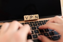 Internet user works on laptop with VPN Virtual Private Network for secure and encrypted connection, anonymously on Internet. Hands on laptop keyboard and letters VPN on cubes.