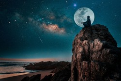 person silhouette sitting on the top of the mountain meditating or contemplating the starry night with Milky Way and Moon background	