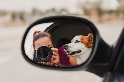 young woman taking a picture with camera on rear mirror of her cute small jack russell dog watching by the window. Ready to travel. Traveling with pets concept