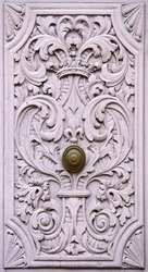 Close-up of a historic courtyard gate with a door handle and ornate wood carvings in dusky pink