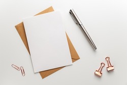 Greeting, wedding or congratulations stationery mockup. Blank sheet of paper on brown envelope, fountain pen and various paper clips on clean desk. Table top view, flat lay, copy space.