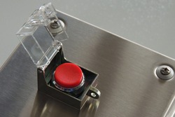 Clean, empty and a round red button with a raised a safety cap. The button is located on a metal box and is ready to use. There are no inscriptions. Close-up. Copy space.